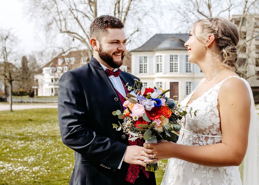 A wedding couple shares a joyful moment outdoors with a vibrant bouquet of pink and purple flowers.