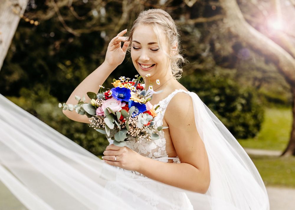 Sunlit wedding scene with bouquet featuring bright blue and red flowers.