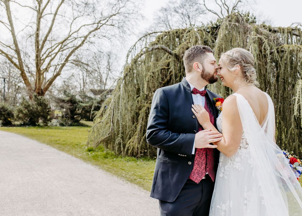 A couple in formal wedding attire shares romantic moments along a tree-lined path.