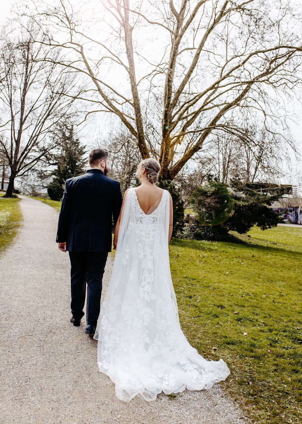 Bride and groom walking along a scenic path through a park with bare winter trees in the background.