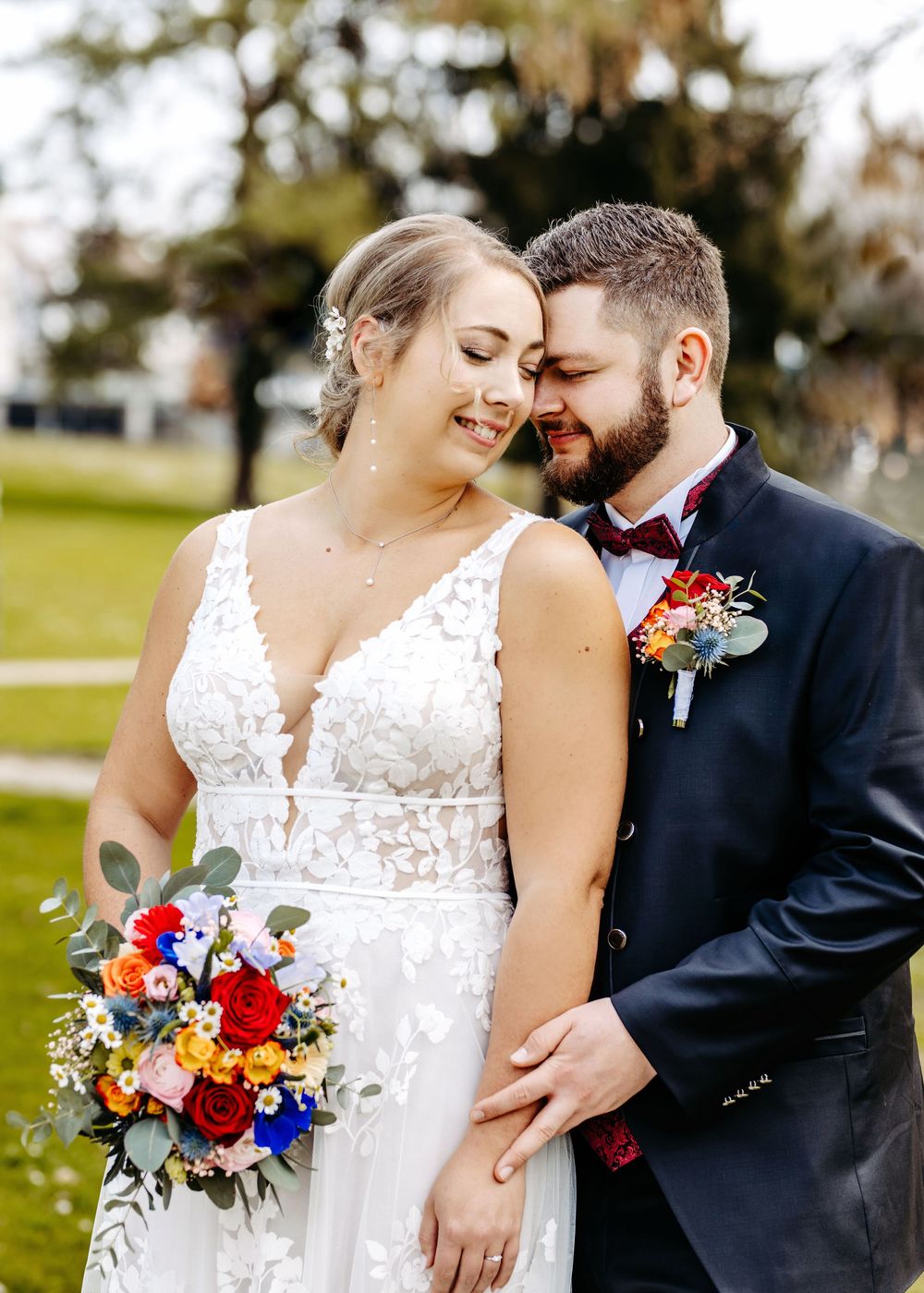 A romantic wedding couple embraces while laughing together in an outdoor garden setting with vibrant flowers.