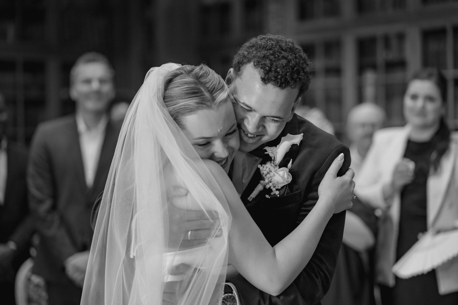 A wedding couple walks hand in hand on a path beside a stately building with a flowing veil trailing behind.