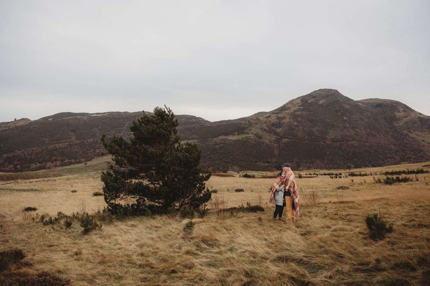 Hikers traverse a rugged mountain landscape under cloudy skies in a scenic panoramic view.
