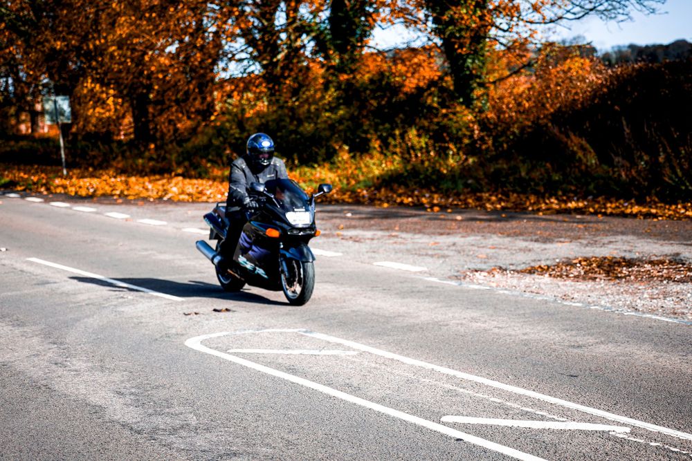 A motorcycle rider leans into a winding mountain road curve surrounded by autumn foliage.