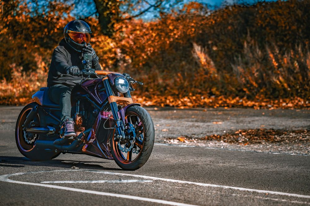 Motorcycle parked on autumn road with orange fallen leaves creating vibrant seasonal backdrop.