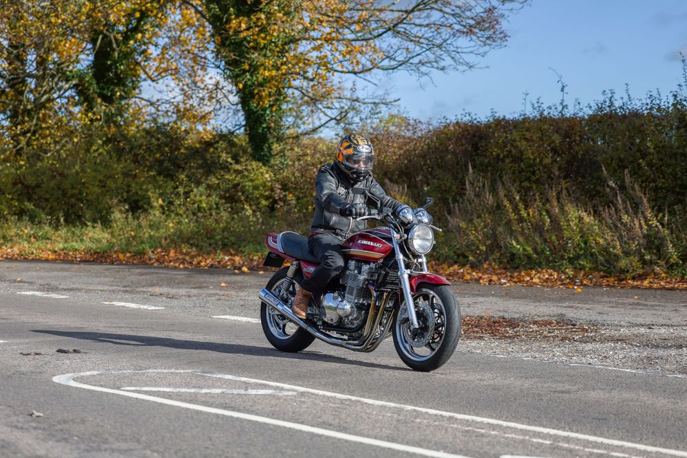 Motorcycle rider leaning into a curve on a winding autumn road with fallen leaves on the pavement.