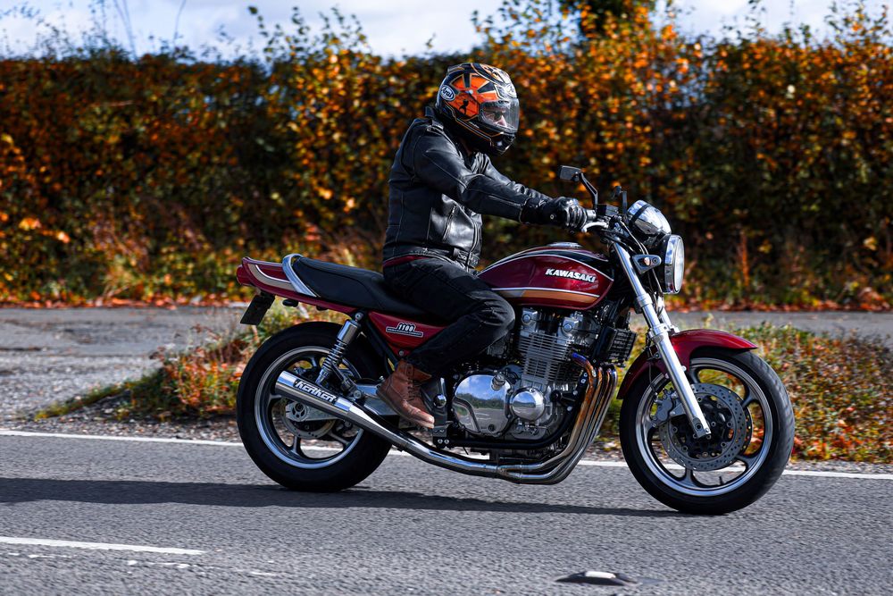 Custom motorcycle cruising on winding road surrounded by orange fall foliage and trees.
