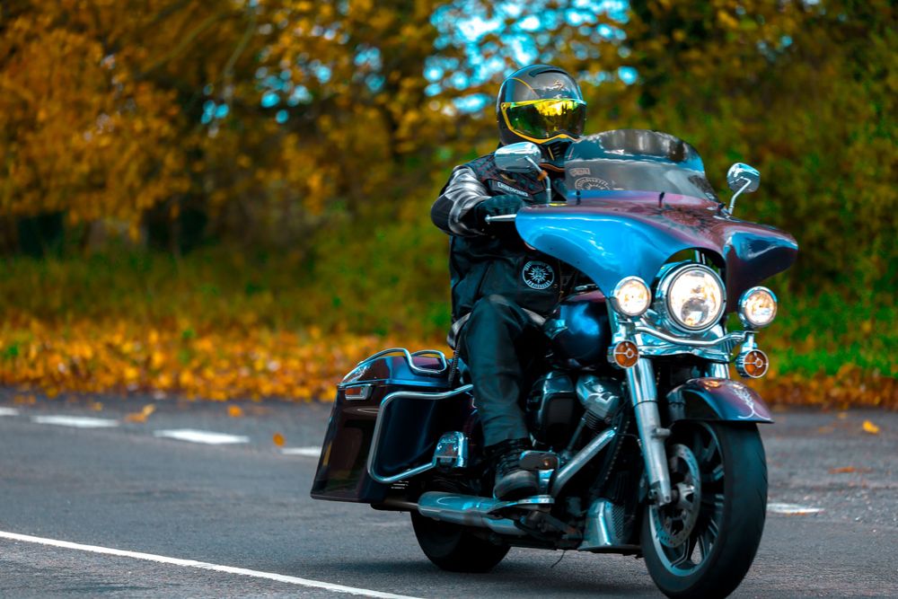 Motorcycle cruising along a curvy road with autumn trees and blue sky in the background.