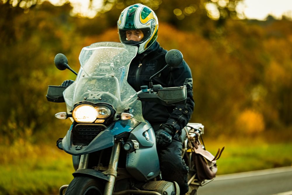 A motorcycle rider travels down a scenic autumn road at sunset with golden light filtering through trees.