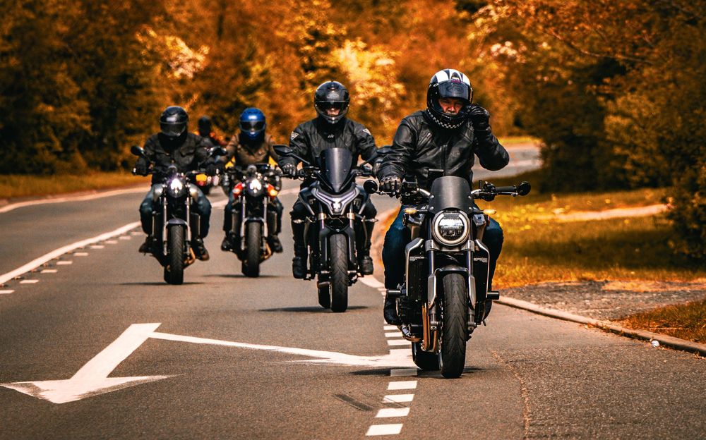 Group of motorcyclists riding in formation on an autumn road with golden foliage and fallen leaves.