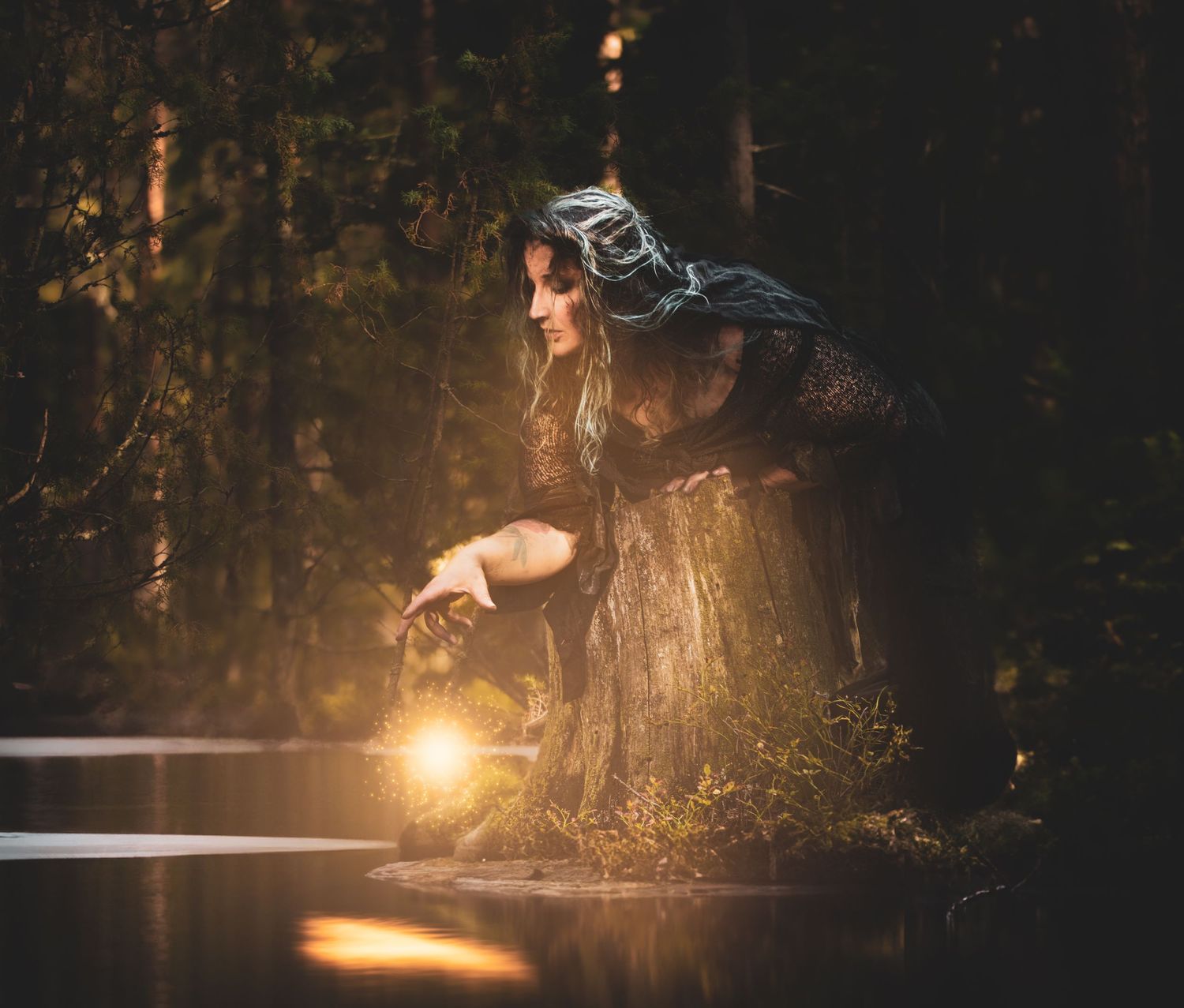 A mystical figure in dark attire holds a glowing lantern by a misty forest pond in moody lighting.