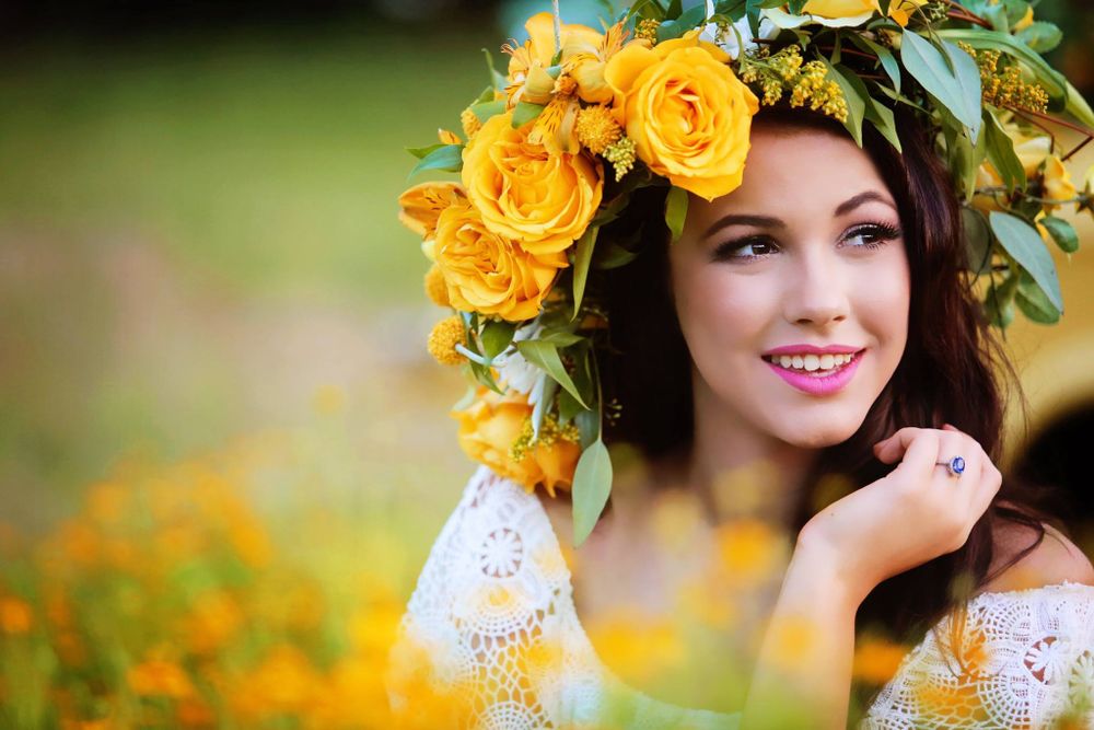 Woman wearing yellow rose crown in white lace dress against sunny garden background.
