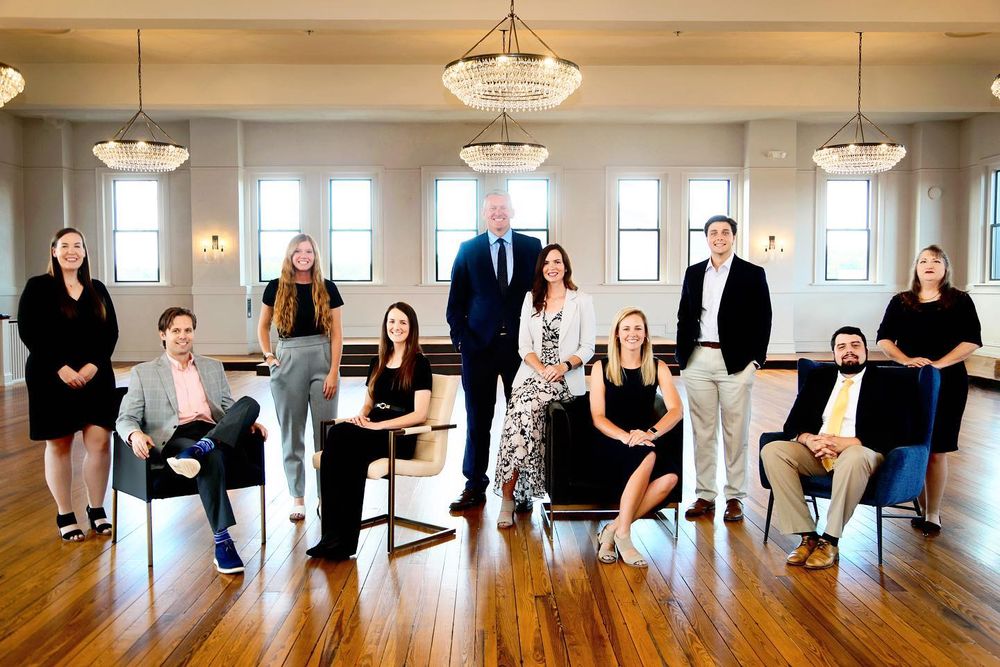 Professional office team photo in an elegant room with hardwood floors and pendant lighting.