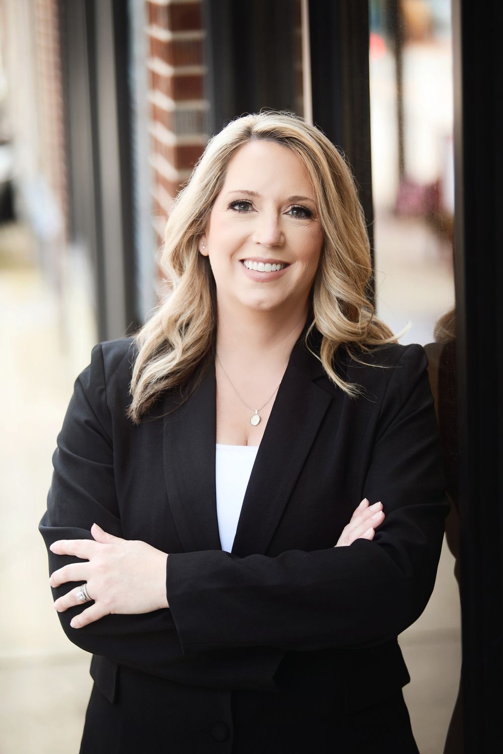 A business professional in a black blazer smiles confidently in an urban setting.