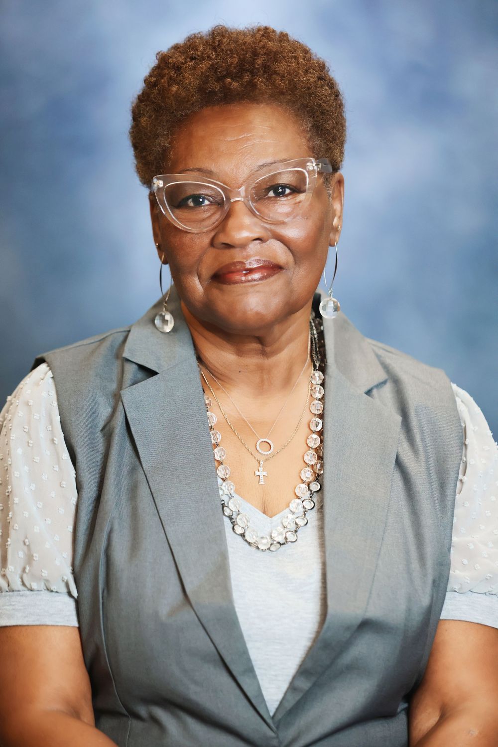 Professional portrait series showing a person in a gray vest and white top wearing glasses and silver jewelry against blue backdrop.