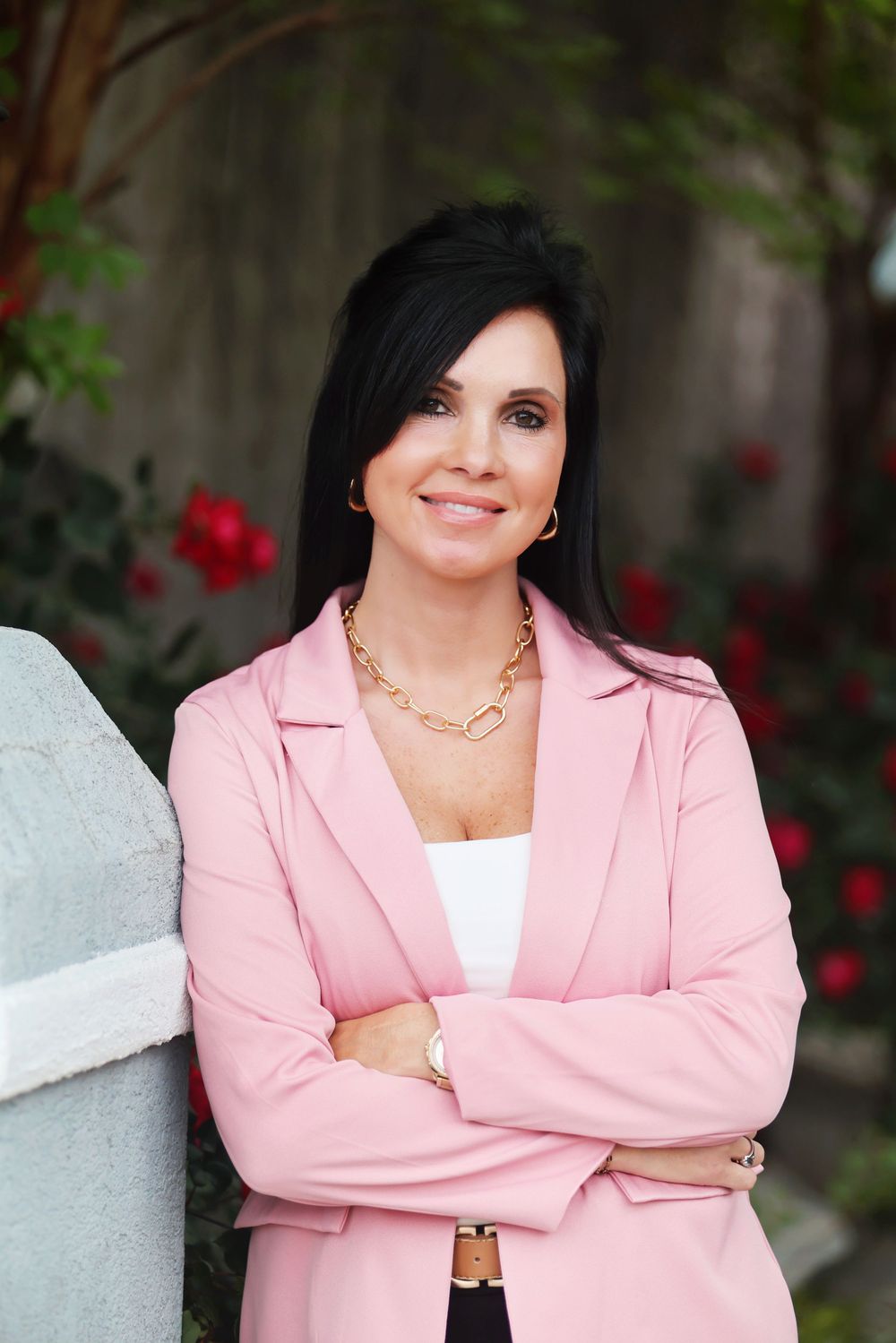Professional portrait series in pink blazer and white top against garden backdrop with red flowers.
