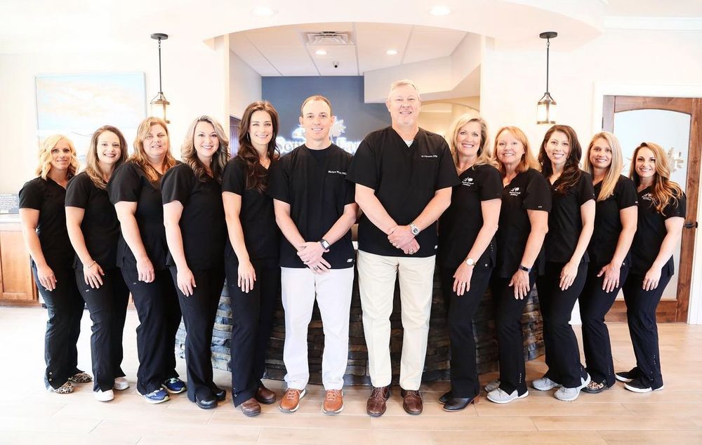 Large group photo of a medical or dental office staff wearing matching black uniforms.