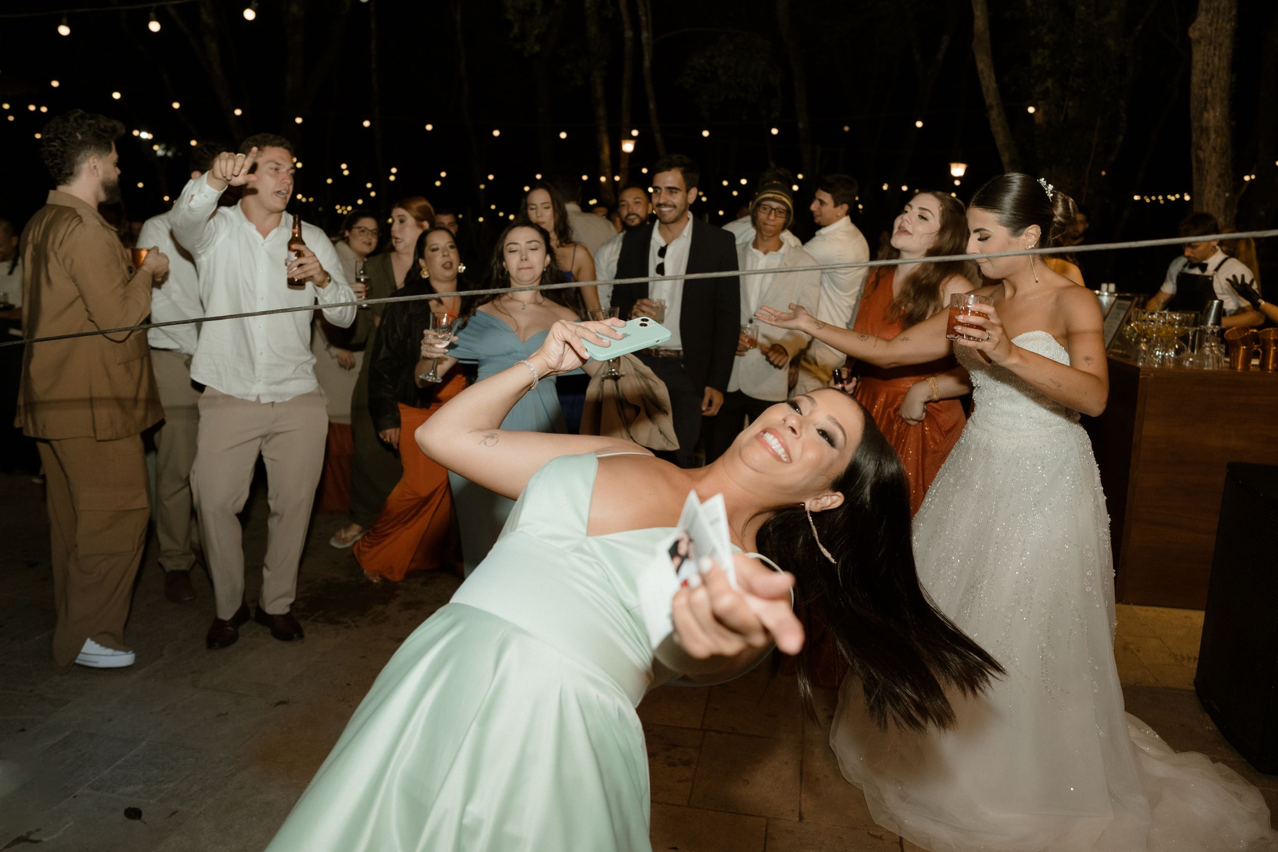 Wedding guests dancing energetically at an outdoor reception under string lights.