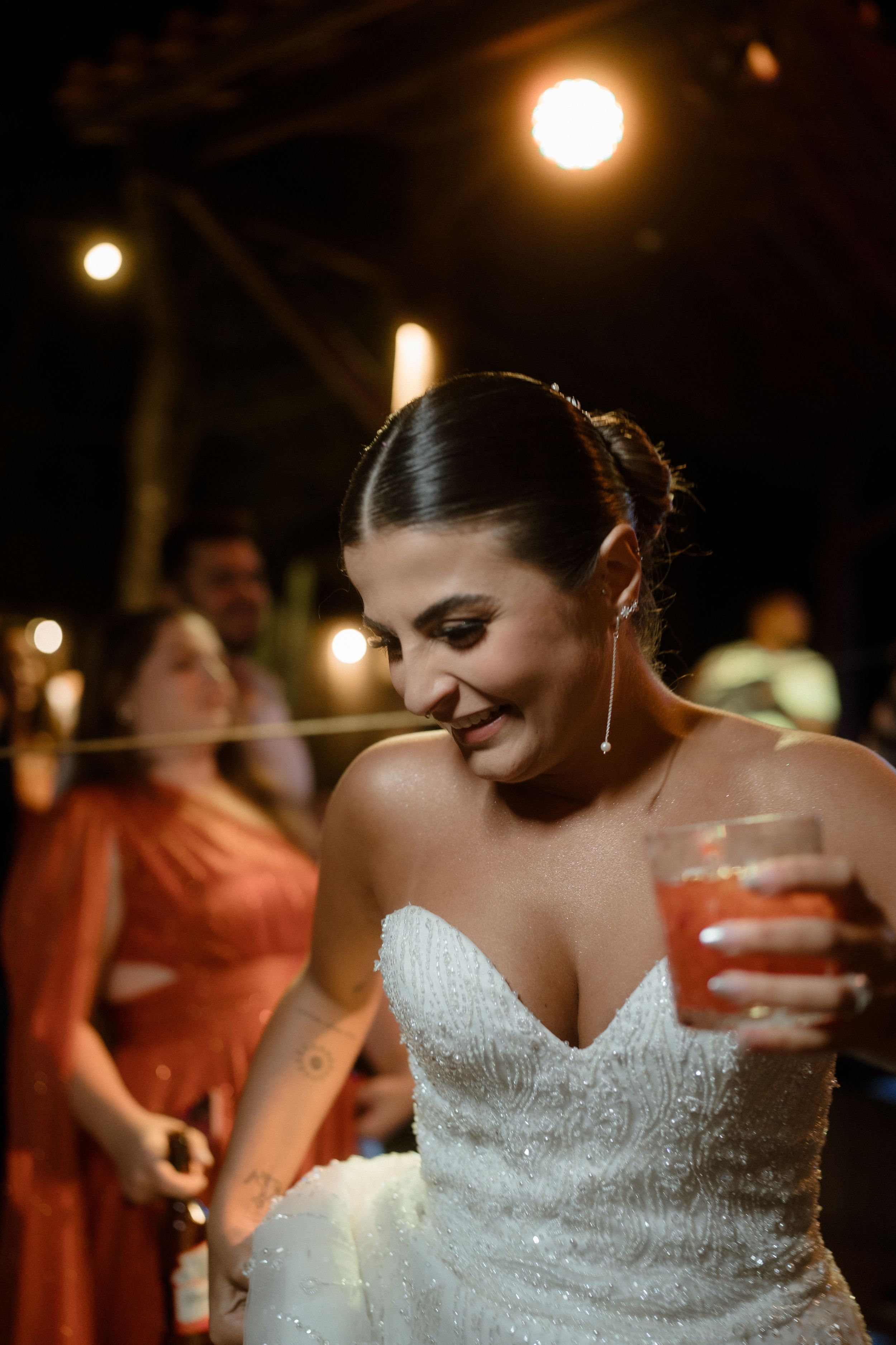 A bride enjoying her wedding reception while holding a festive cocktail under warm lighting.