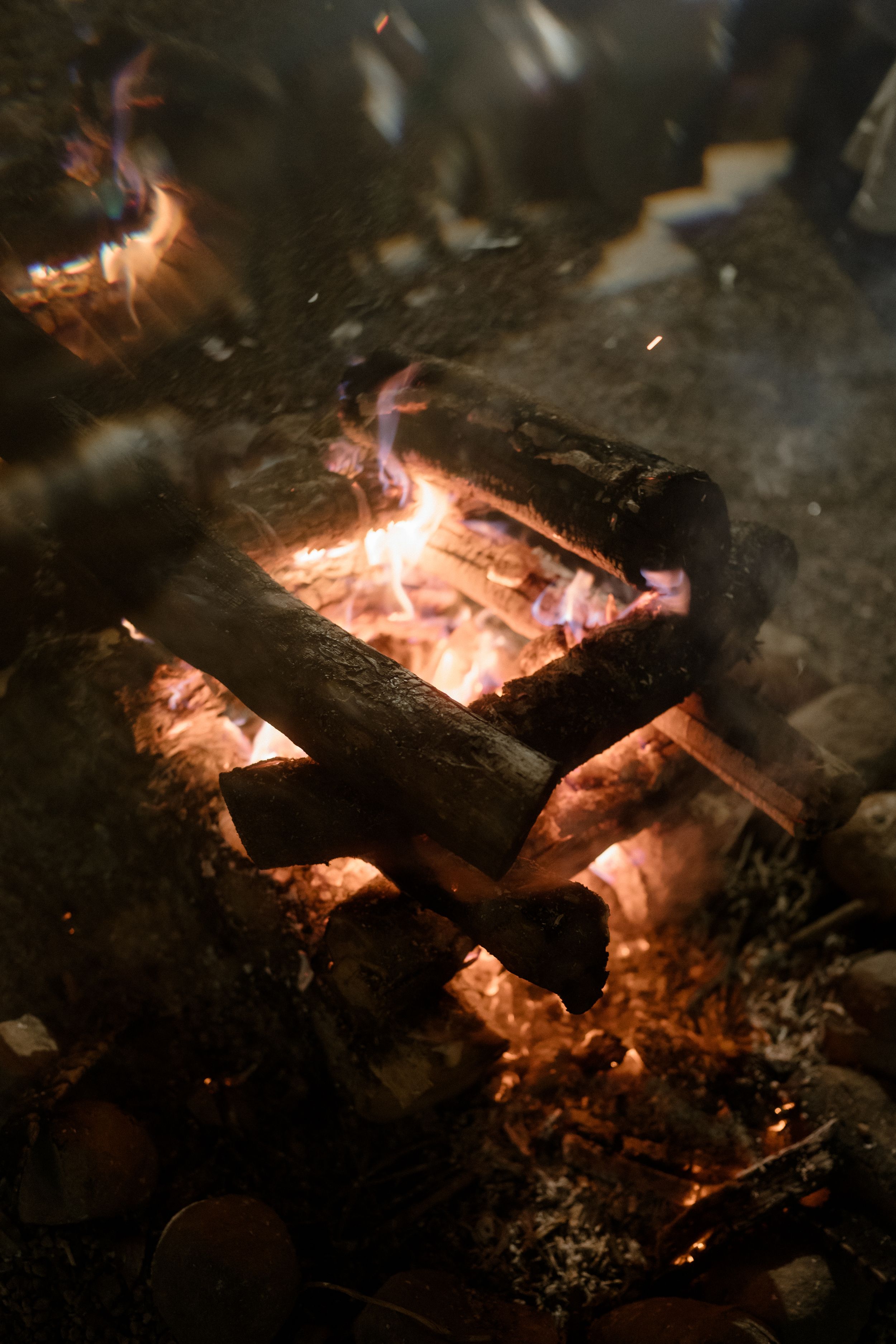 Glowing wood embers and flames in a nighttime bonfire.