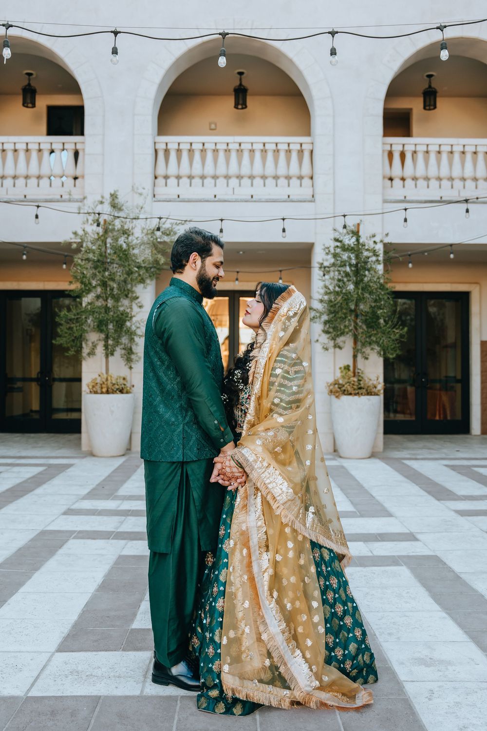 Elegant couple in South Asian wedding attire photographed in white courtyard with arches.