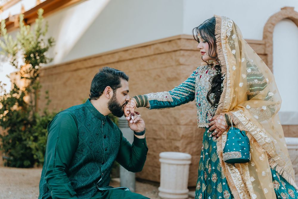 A couple in emerald green and turquoise outfits pose together in an outdoor setting.