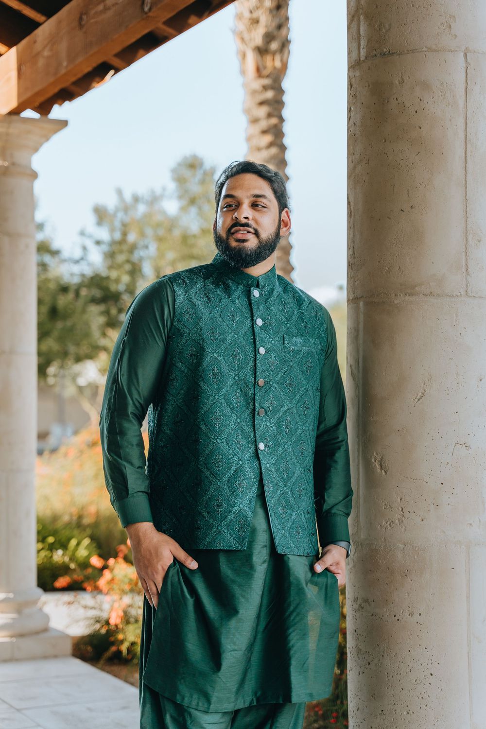 Person in an emerald green traditional outfit poses against white stone columns.