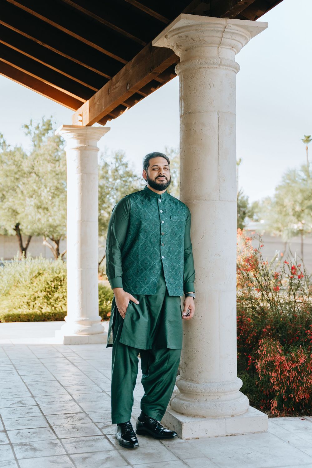 Person wearing emerald green traditional attire poses between stone columns outdoors.