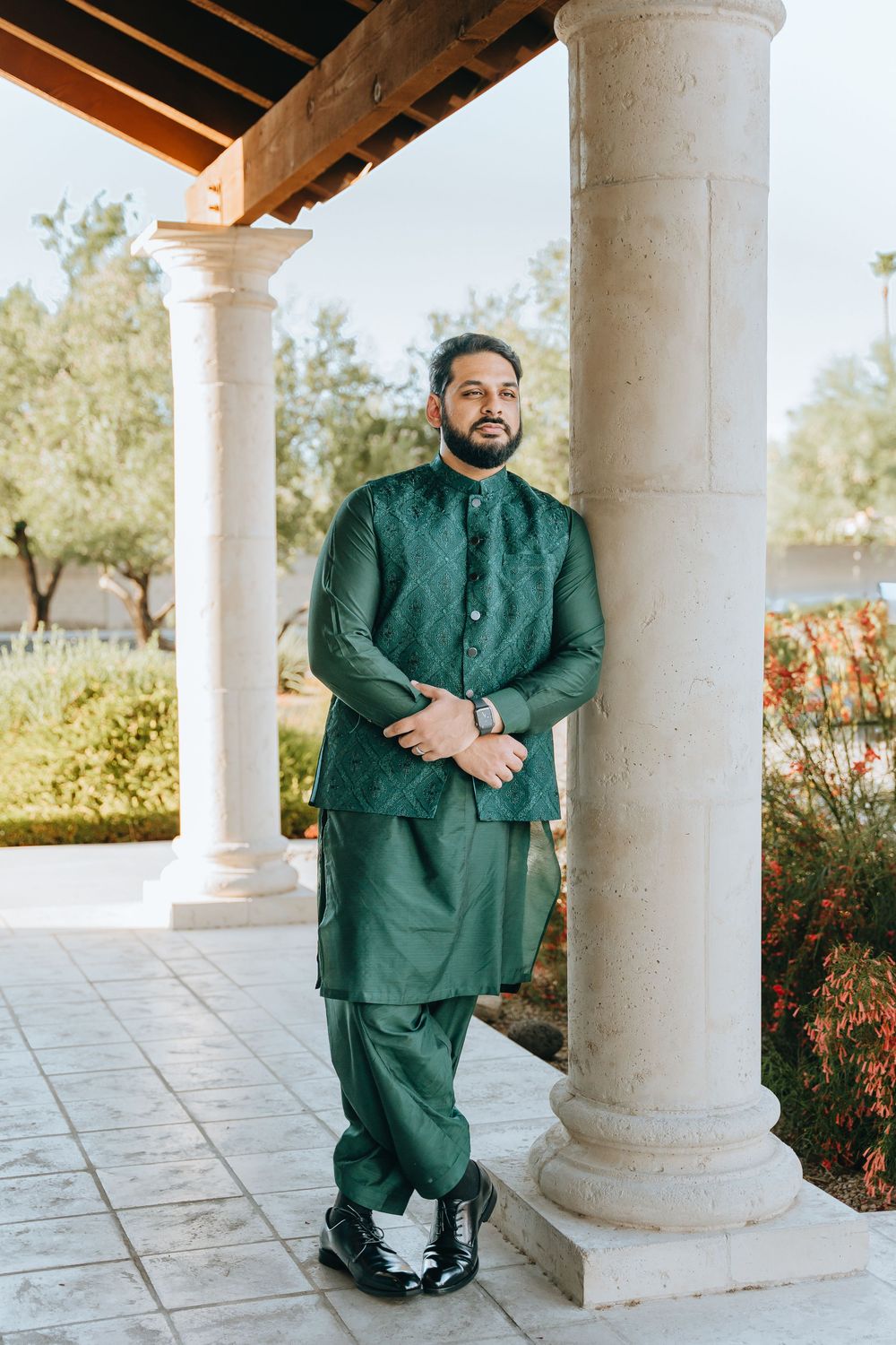 Person in emerald green South Asian attire poses between white stone columns.