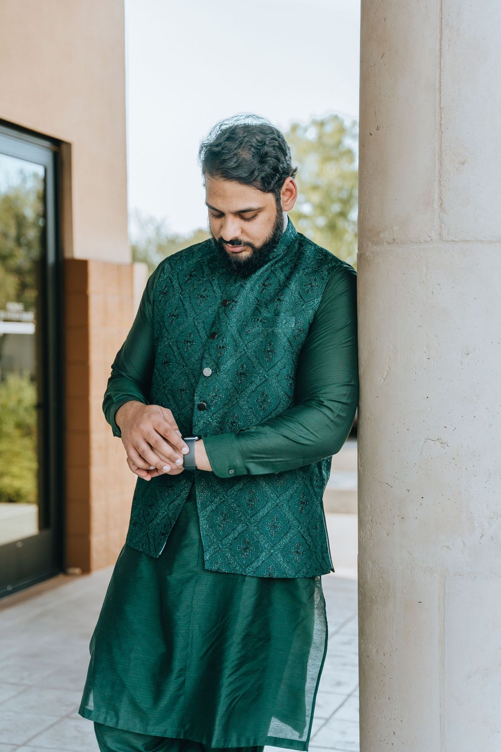 Person in emerald green traditional wear poses against architectural columns.