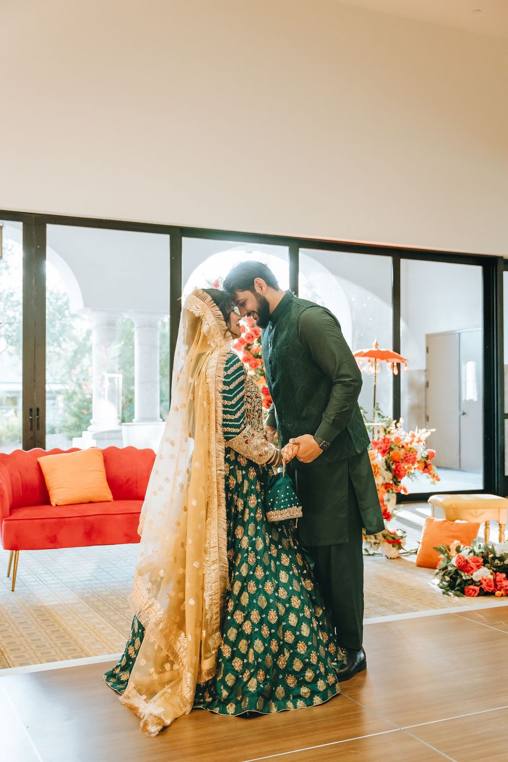 Couple in traditional South Asian attire pose in a modern interior with orange decor.