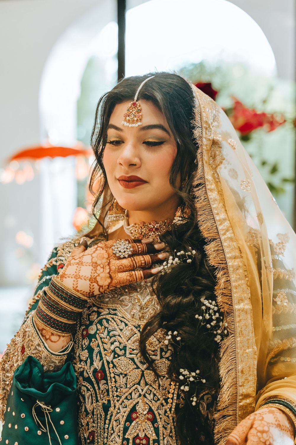 Close-up details of bride in emerald and gold embroidered South Asian wedding dress with intricate jewelry.
