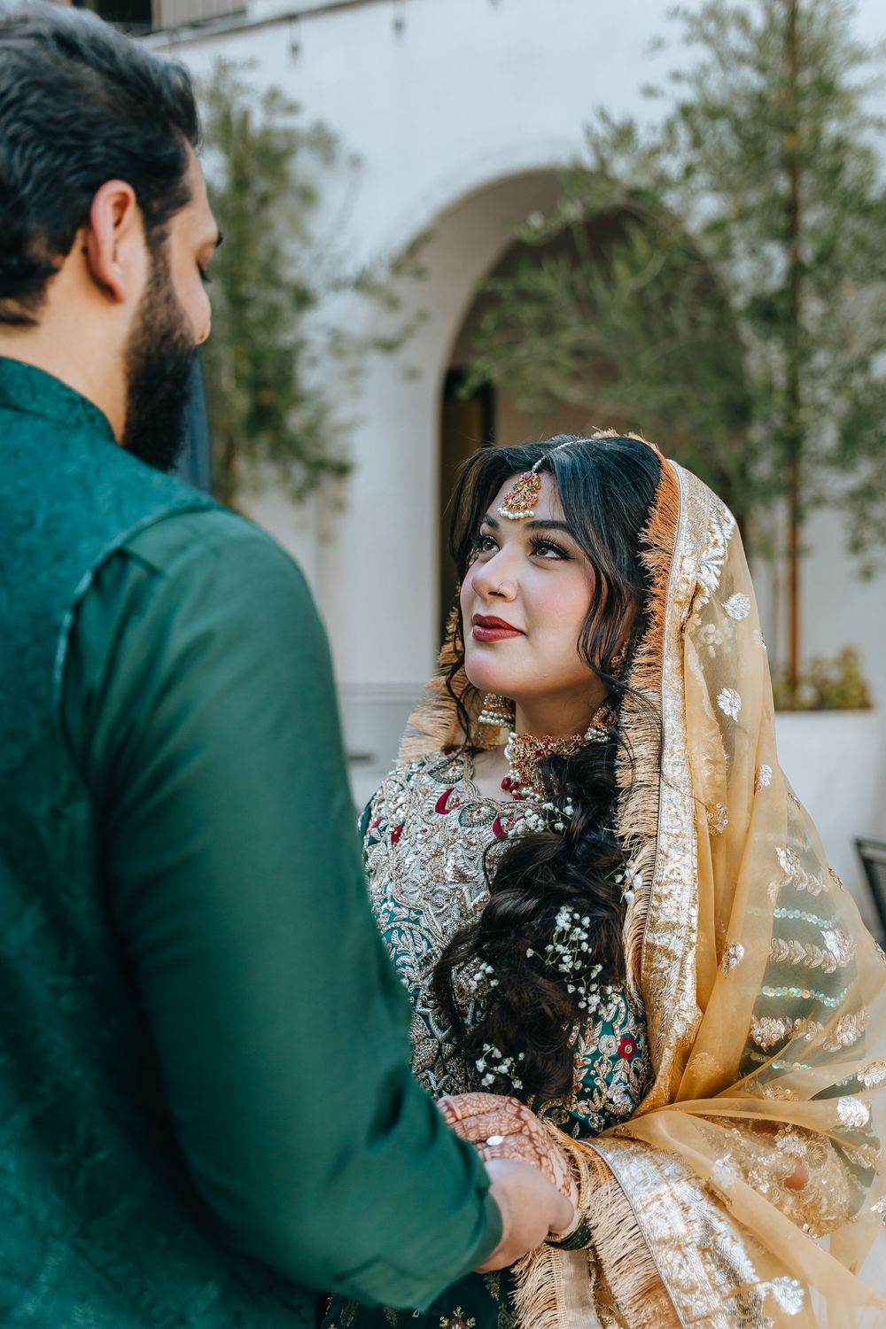 Traditional South Asian wedding couple in emerald and gold attire pose together.