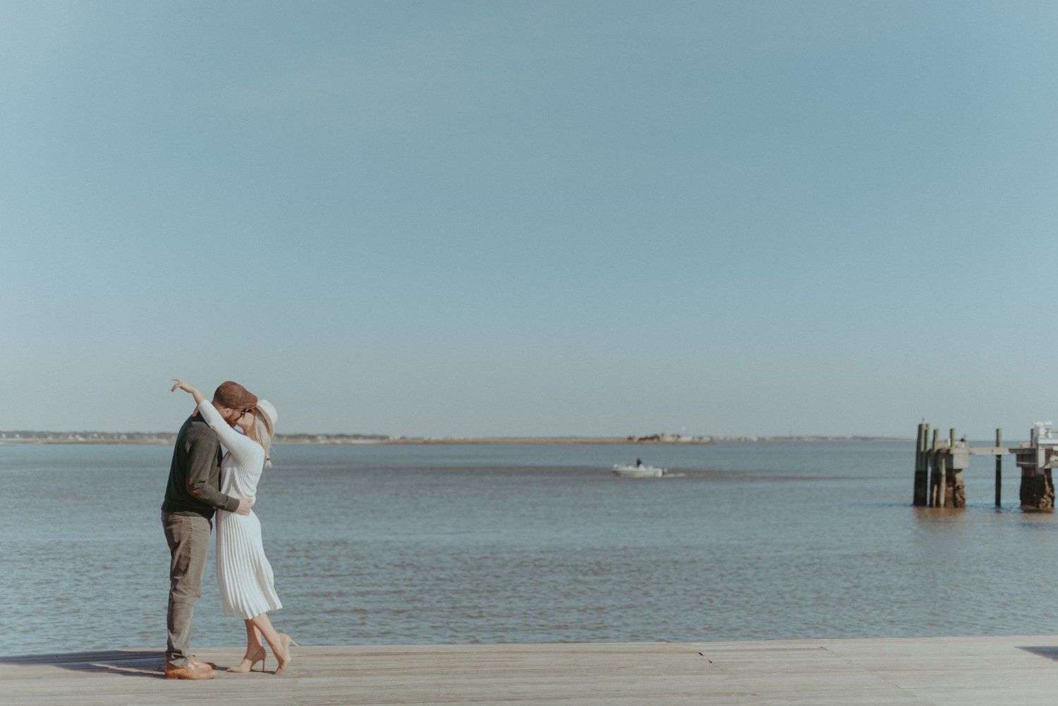 A couple are kissing with the ocean behind them.
