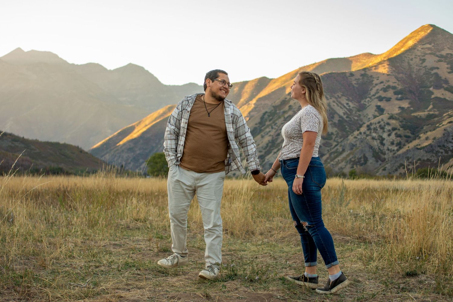couple laughs and hold hands in front of 
Utah mountains.
