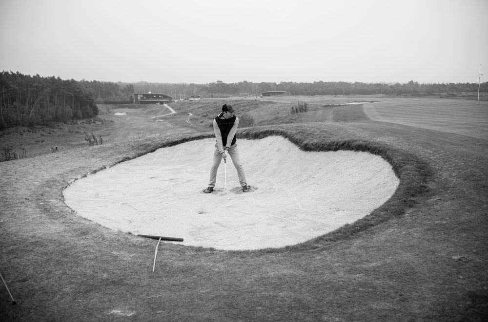 Golfer stands in a sand bunker on a remote golf course in black and white.
