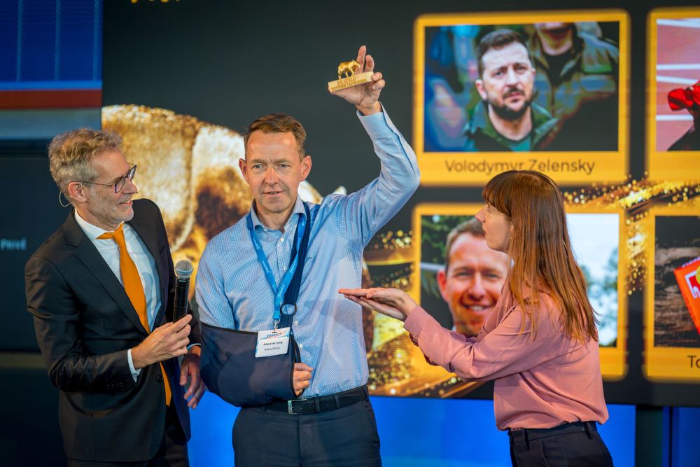 Group celebrates enthusiastically during corporate event with display screens in background.