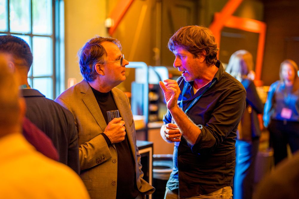 Two individuals engaged in animated conversation at dimly lit networking event.