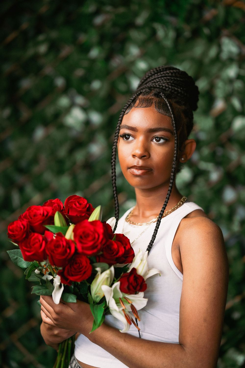 Artistic portrait holding red roses and white lilies against green leaf background in casual attire.