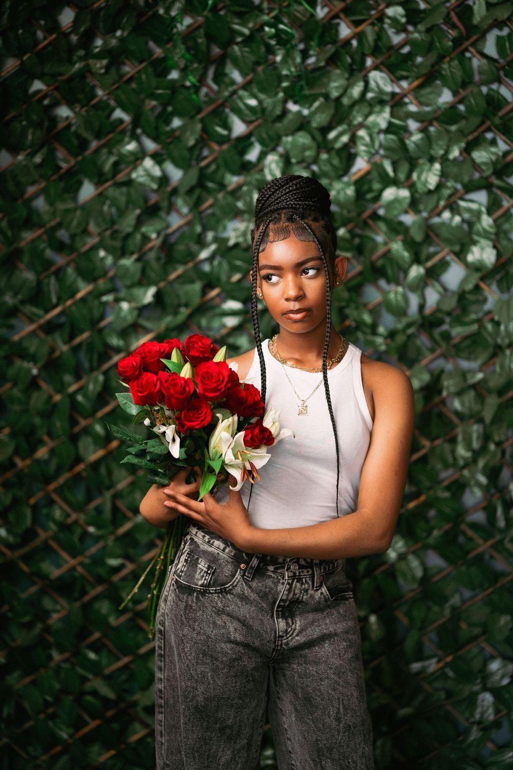Stylish portrait with vibrant red roses and white lilies against greenery wearing casual denim.