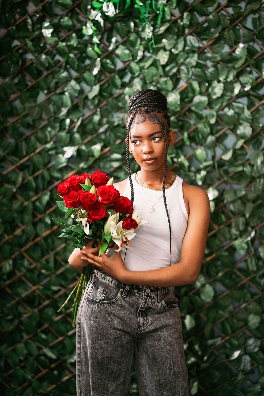Fashion portrait with red rose bouquet against textured green foliage wall.