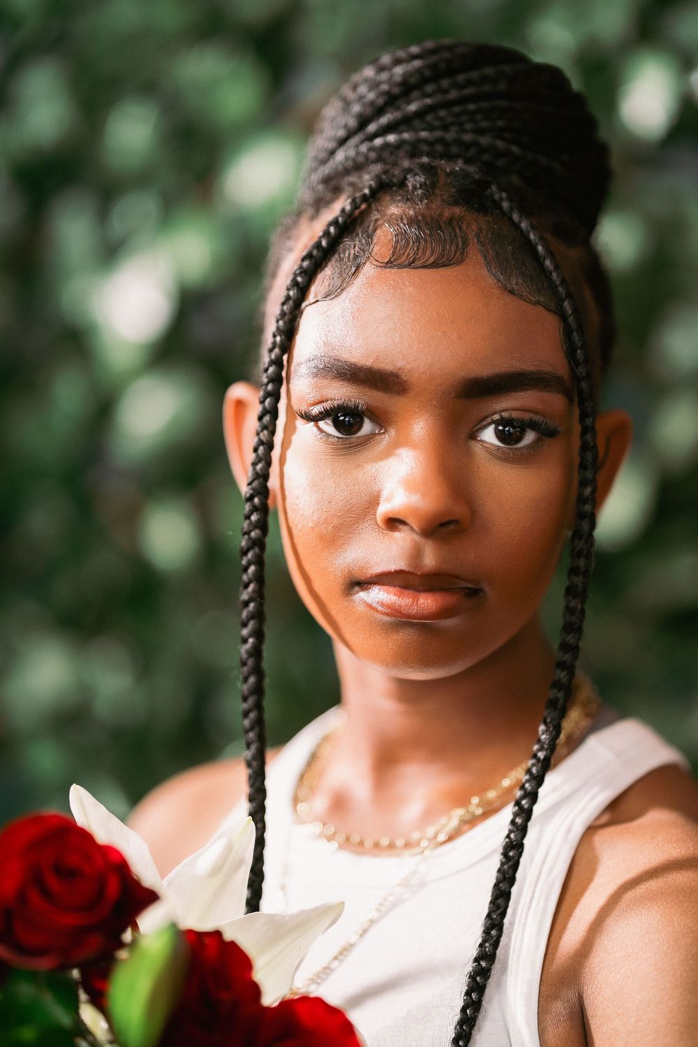 Beauty portrait featuring braided hairstyle and red rose against green background.