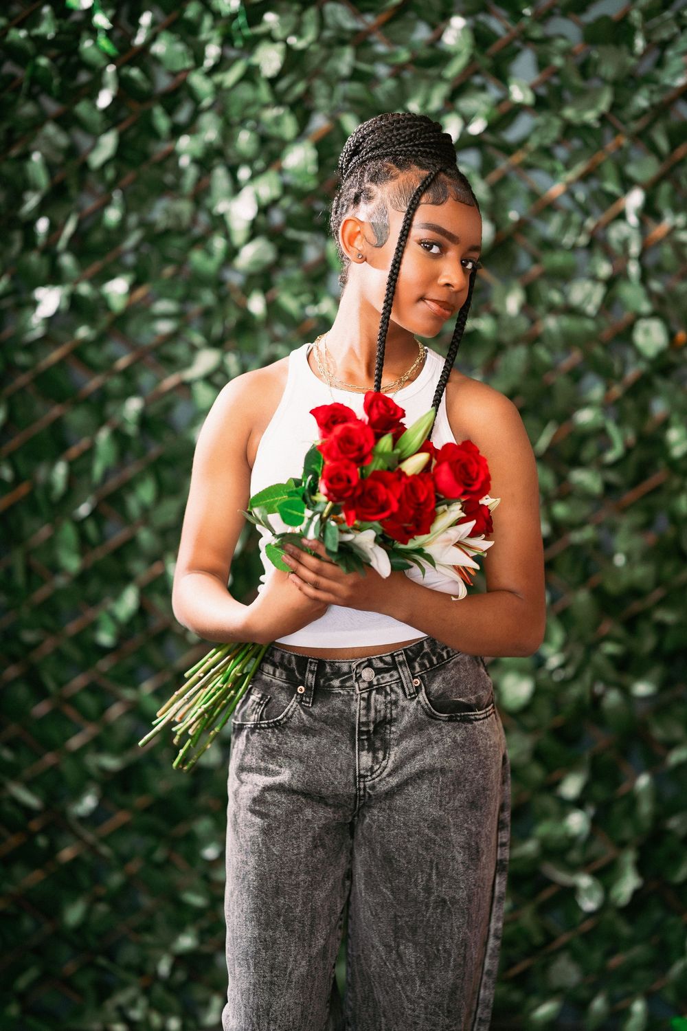 Model in casual attire holding fresh red roses and white lilies against green backdrop.