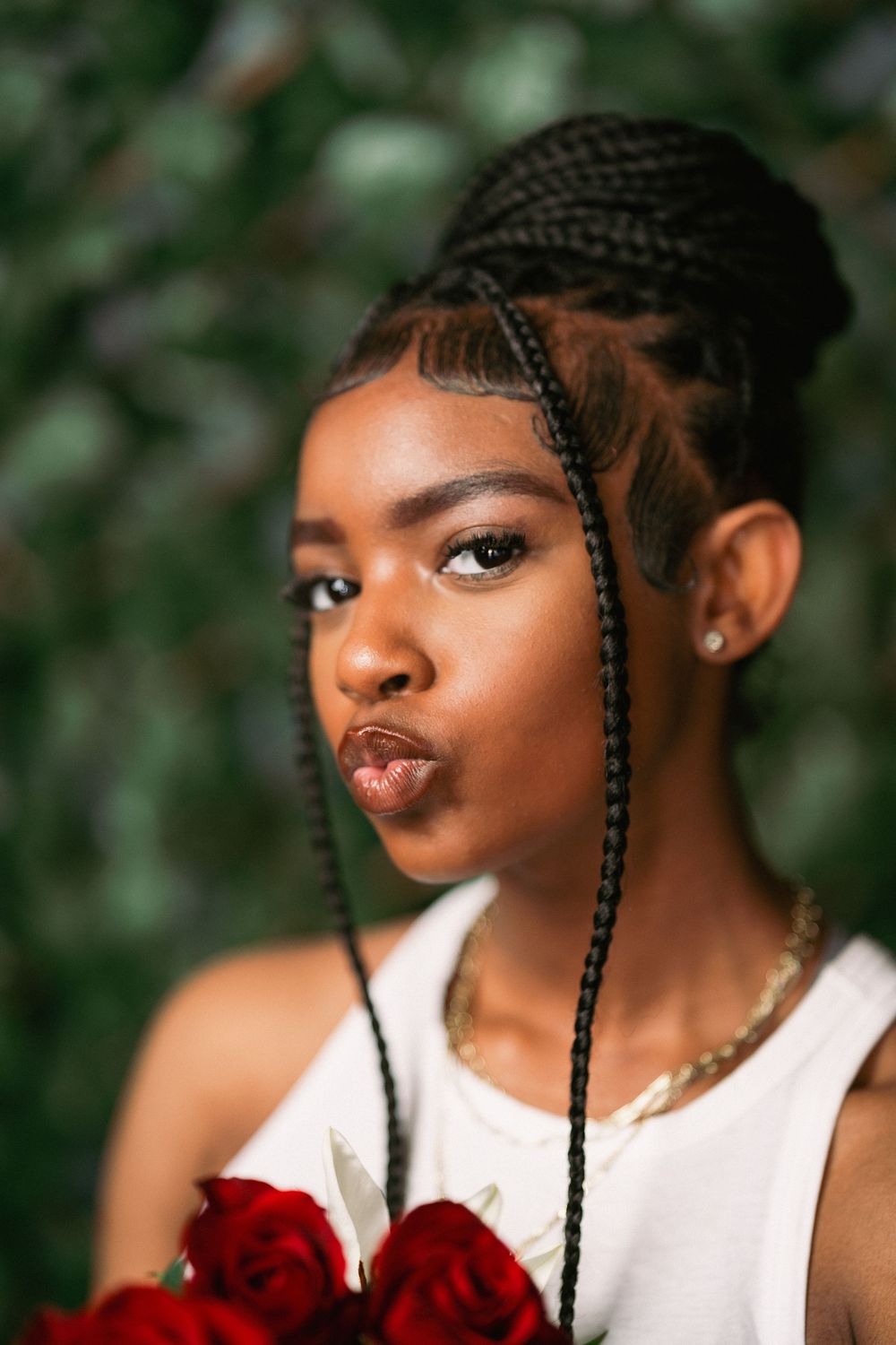 Close-up beauty portrait with braided hairstyle and red roses against green background.