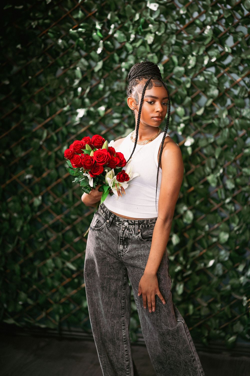 Portrait of model in casual wear holding red roses against leafy green background.