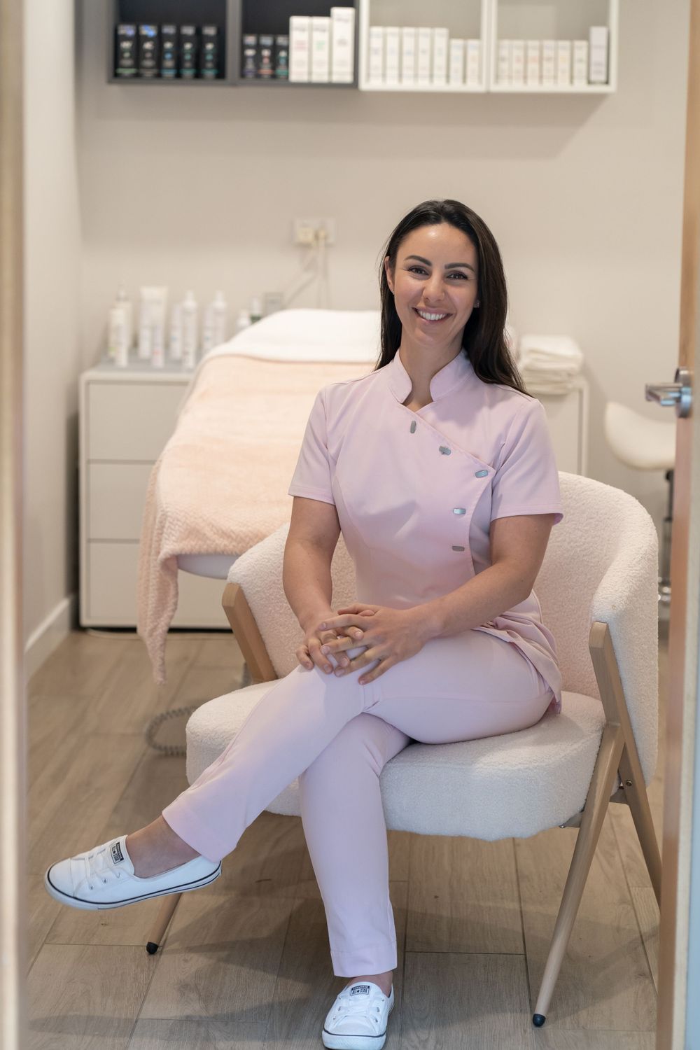 Professional esthetician in pink uniform sitting in modern spa treatment room.