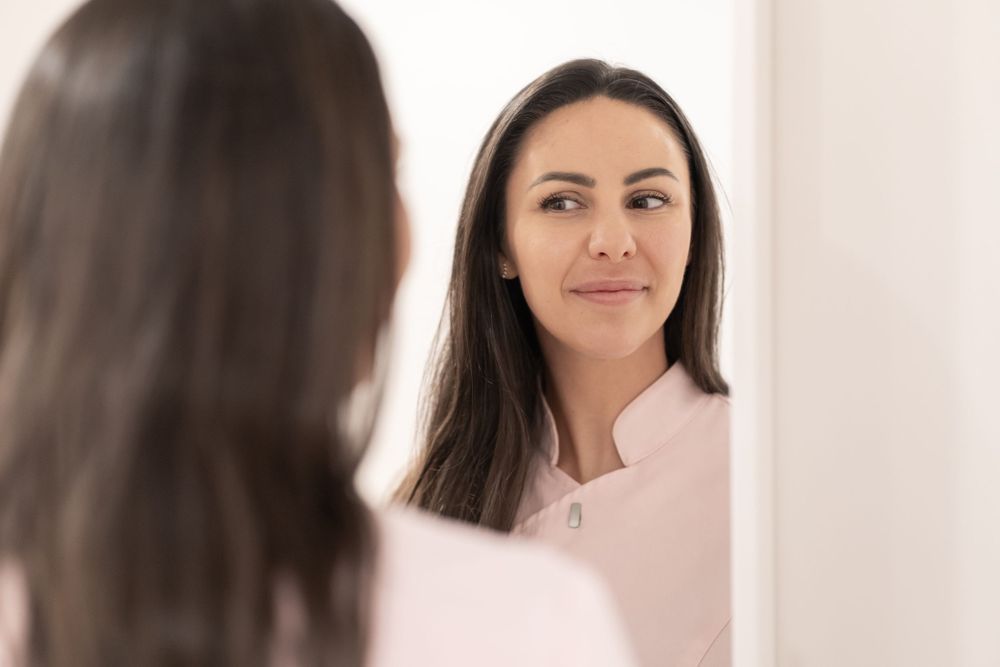 Beauty professional in pink uniform reflects in mirror during skincare consultation.
