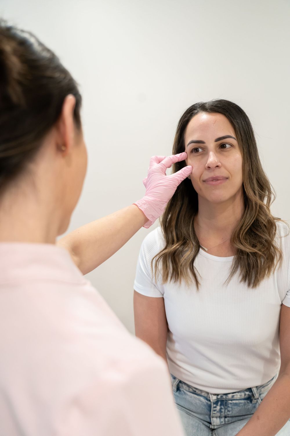 Aesthetic practitioner examining client's face while wearing pink protective gloves.
