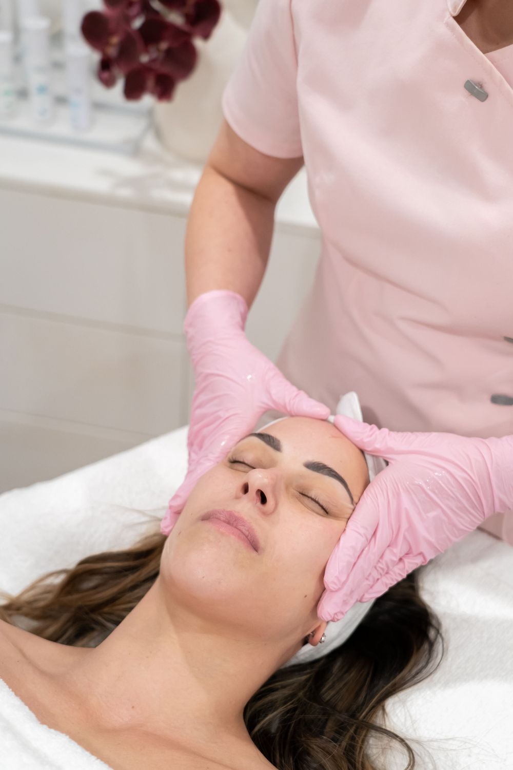 Gentle facial massage being performed with pink medical gloves in spa setting.