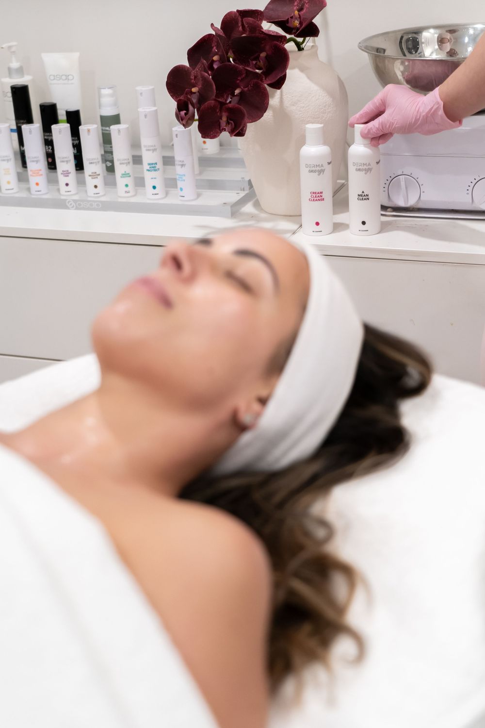 Spa treatment setup with skincare products and orchids on display near resting client.